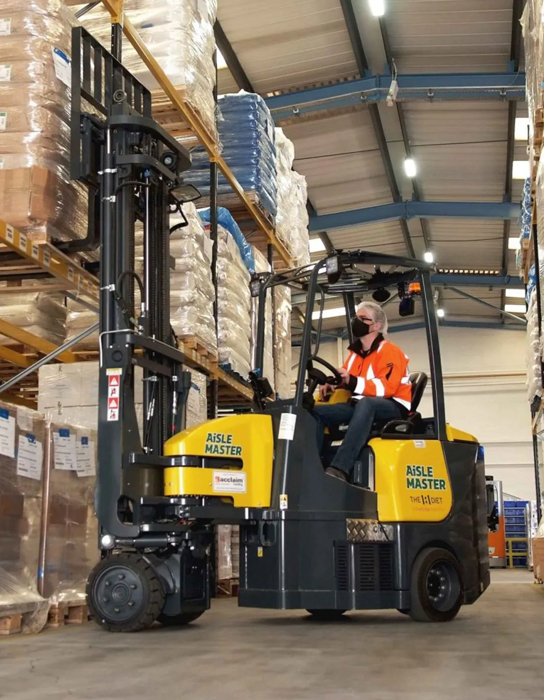 Operator driving an Aisle Master articulated forklift down a warehouse racking aisle