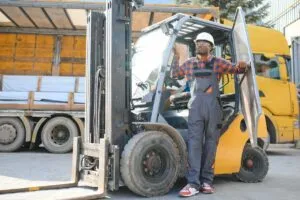 Portrait of a happy African American male worker driving forklift at workplace